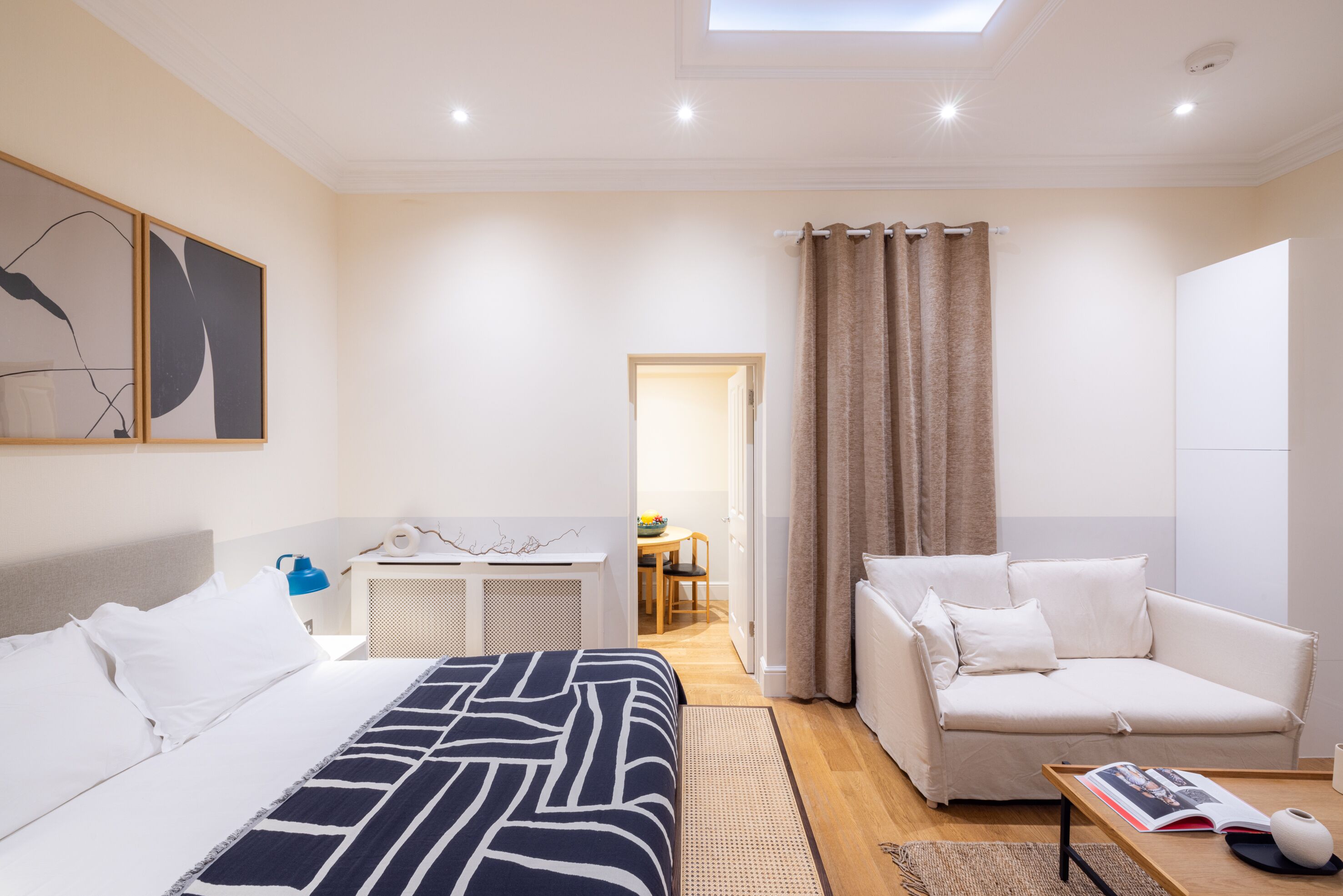 Quarto de hotel moderno com uma cama, um sofá, uma mesinha e vista para o corredor.