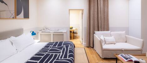Een moderne hotelkamer met een bed, een bank, een tafeltje en uitzicht op de gang.