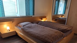 Moderni sänky, jossa on pääty, yöpöytä lampun kanssa ja suuri peili sängyn yläpuolella.