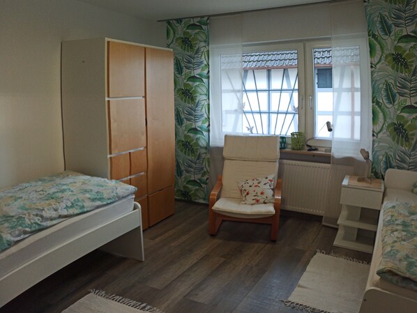 Un dormitorio con cama, armario, silla y escritorio con ventana.