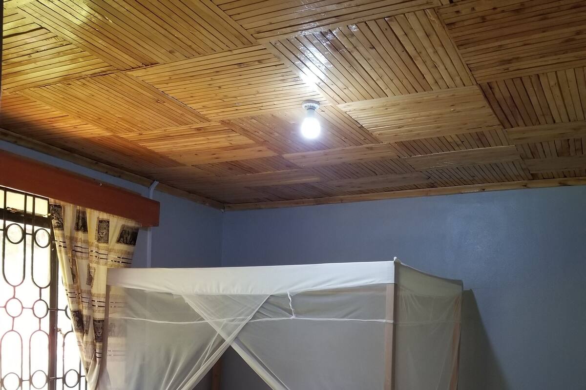 A room with a wooden ceiling, a bed with a mosquito net, a table, and chairs.