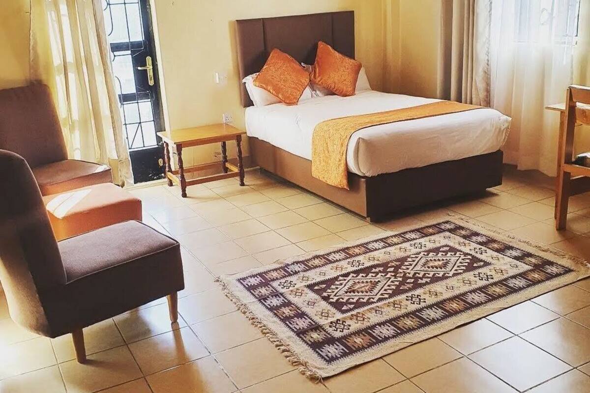 A hotel room with a bed, a chair, a nightstand, a rug, and a window with curtains.