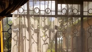 A room with a bed, a bench, and a window with decorative curtains. - Mataman Gardens (Naivasha)