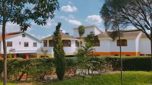 A residential area with white houses, some with orange trim, surrounded by greenery and trees. - Mataman Gardens (Naivasha)