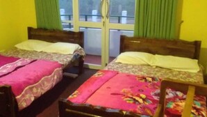 Una habitación con dos camas de madera, cada una con una colcha de motivos florales, y una ventana con cortinas verdes.