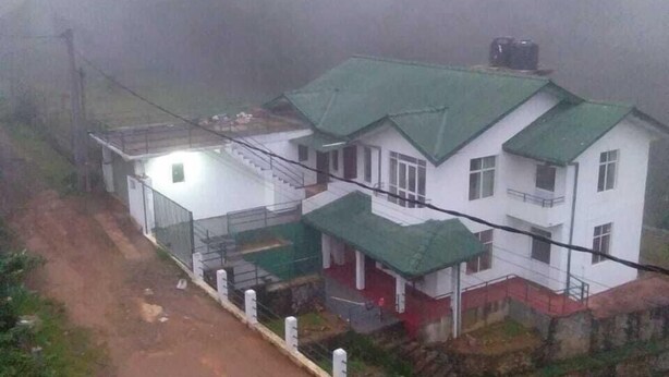 Un edificio blanco con techo verde, rodeado de vegetación y un ambiente brumoso.