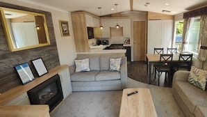 A compact living space with a kitchenette, a sofa, a dining table, and a fireplace. - Osprey Static Caravan - 2 Bedroom - No Pets (Prenteg)