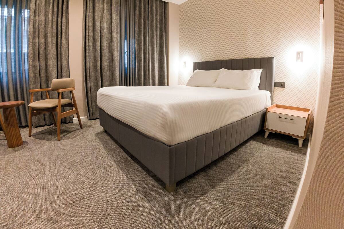 A neatly arranged hotel room with a large bed, a chair, a small table, and a nightstand.