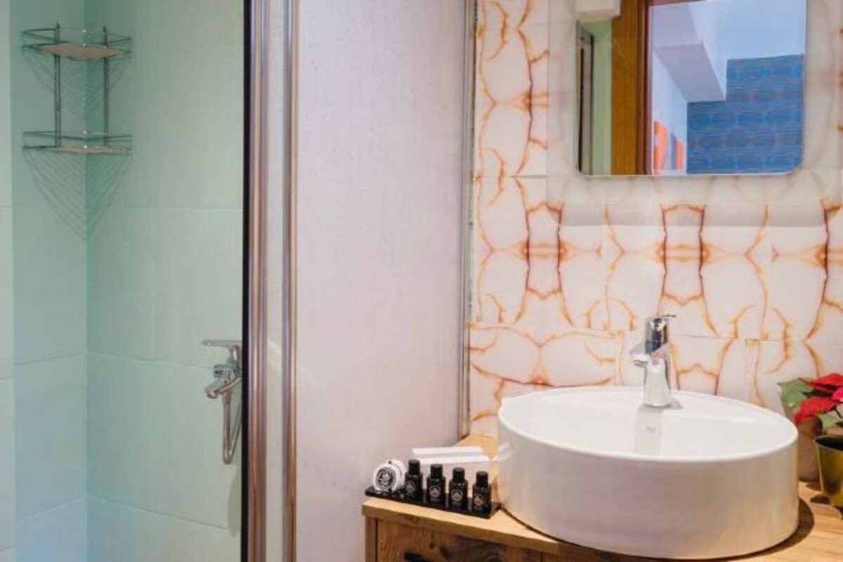 Ein Badezimmer mit einem weißen Waschbecken, einer Holzausstattung, einer Duschkabine aus Glas und einer Wand mit Marmormuster.