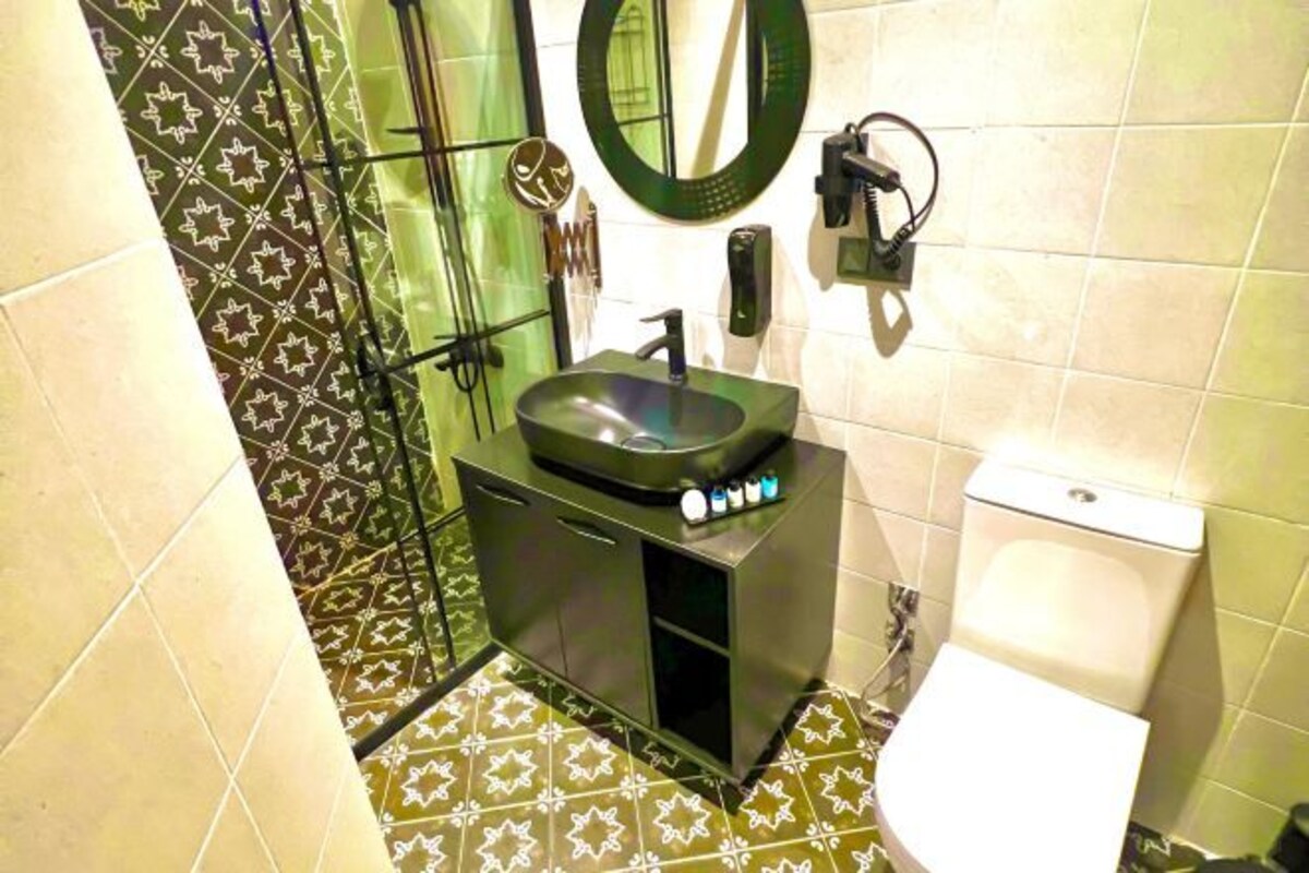 Ein Badezimmer mit einem schwarzen Waschbecken, einer Toilette und einer Duschkabine mit gemusterten Fliesen.