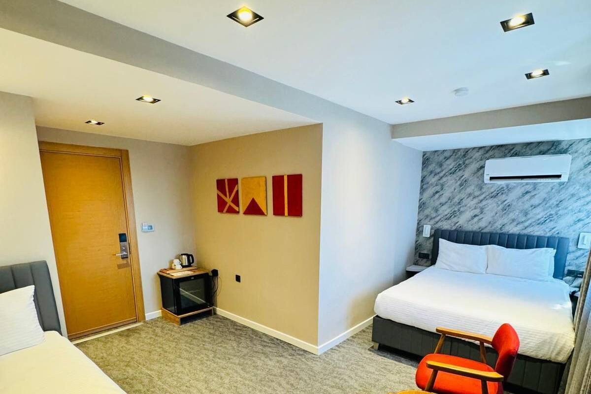 A hotel room with two beds, a desk, two chairs, a small table, a wall-mounted air conditioner, and a door.