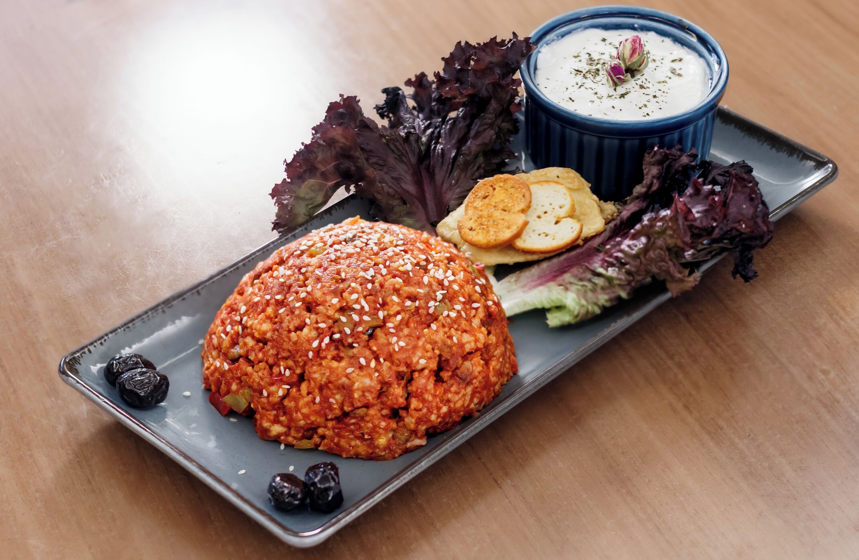 Un plato con un recipiente cubierto de semillas de sésamo, un tazón azul de salsa, y lechuga con galletas.