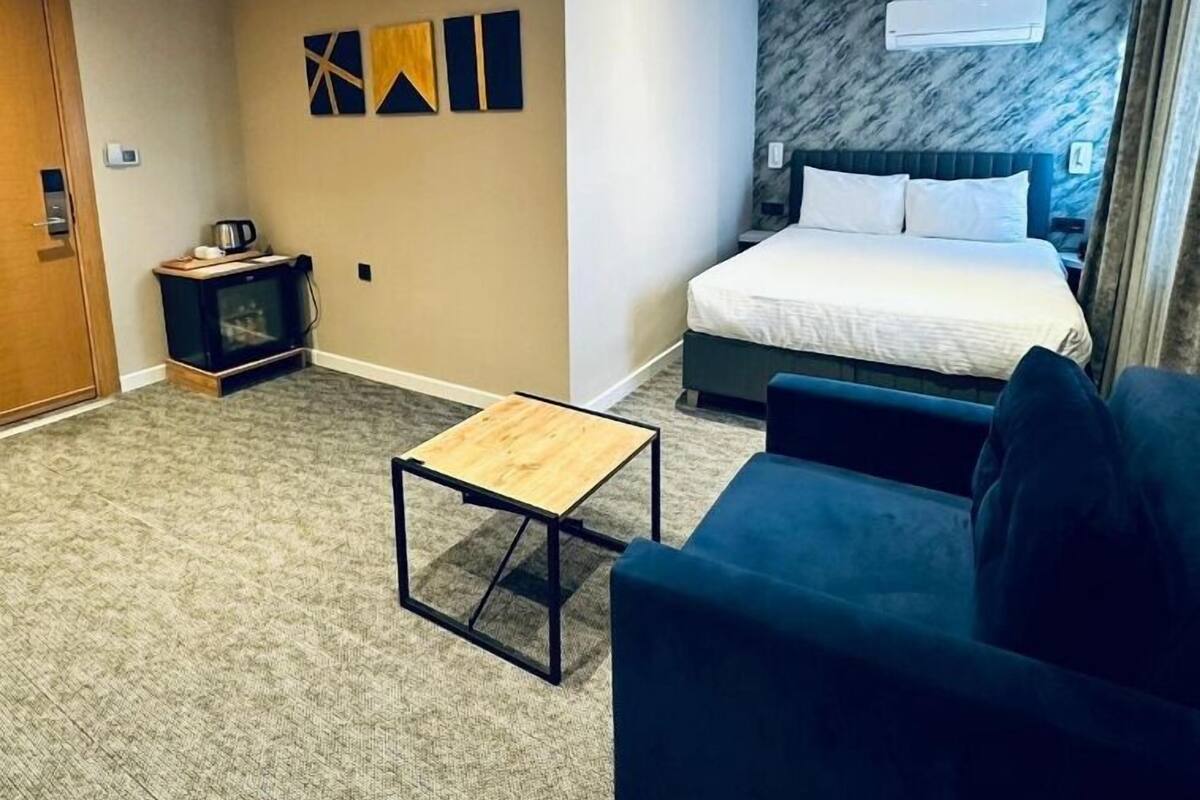 A modern hotel room with a bed, a small table, a TV, and a wall-mounted air conditioner.