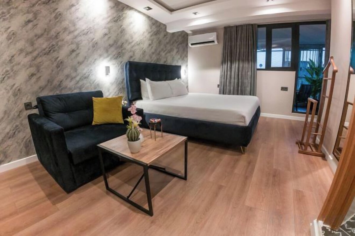 Habitación de hotel con cama, sofá, una mesita de centro y vistas al exterior.