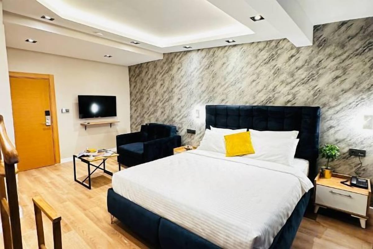 Una habitación de hotel moderna con una cama grande, un televisor de pantalla plana, un escritorio y una silla.
