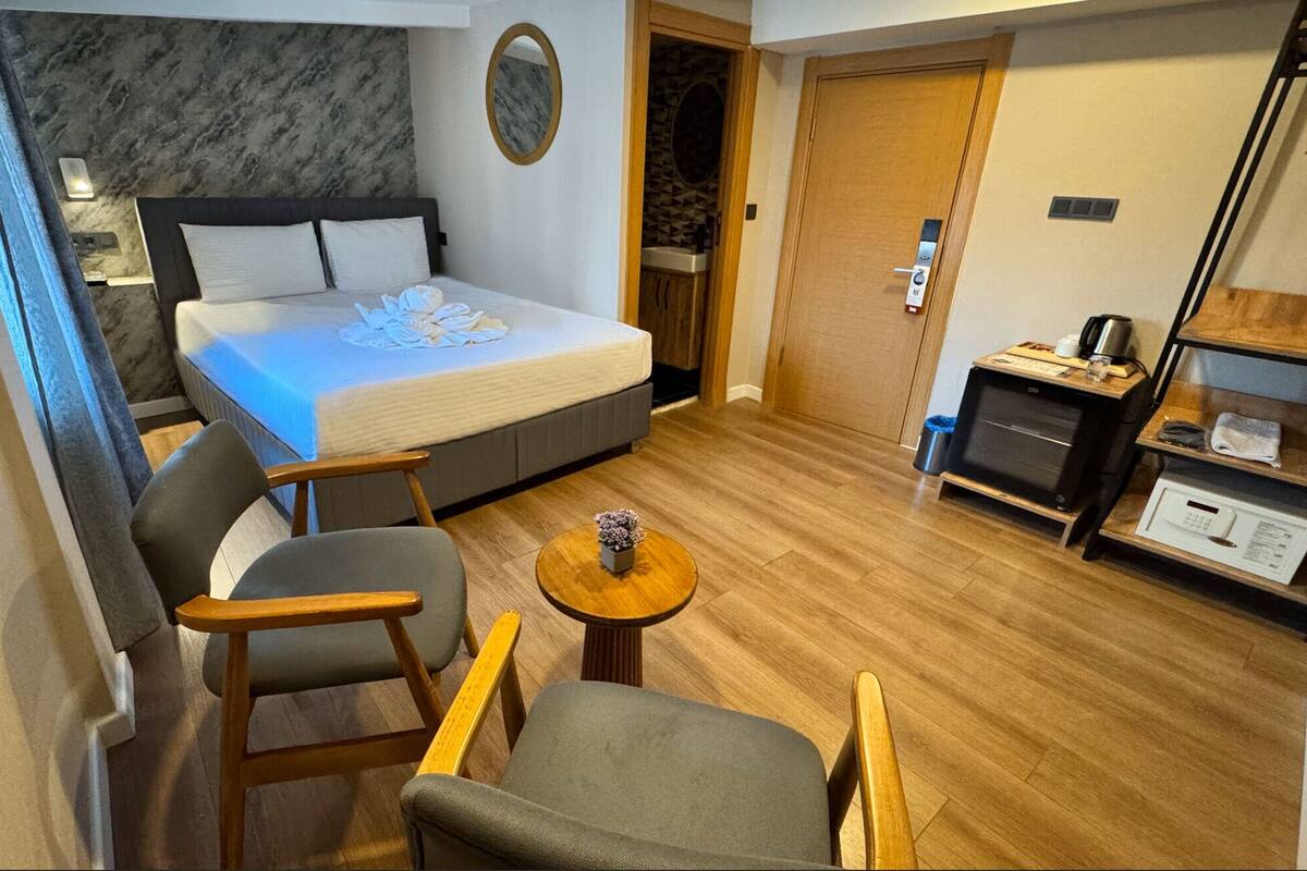 A compact hotel room with a bed, two chairs, a small table, a desk with a computer, and a wardrobe.