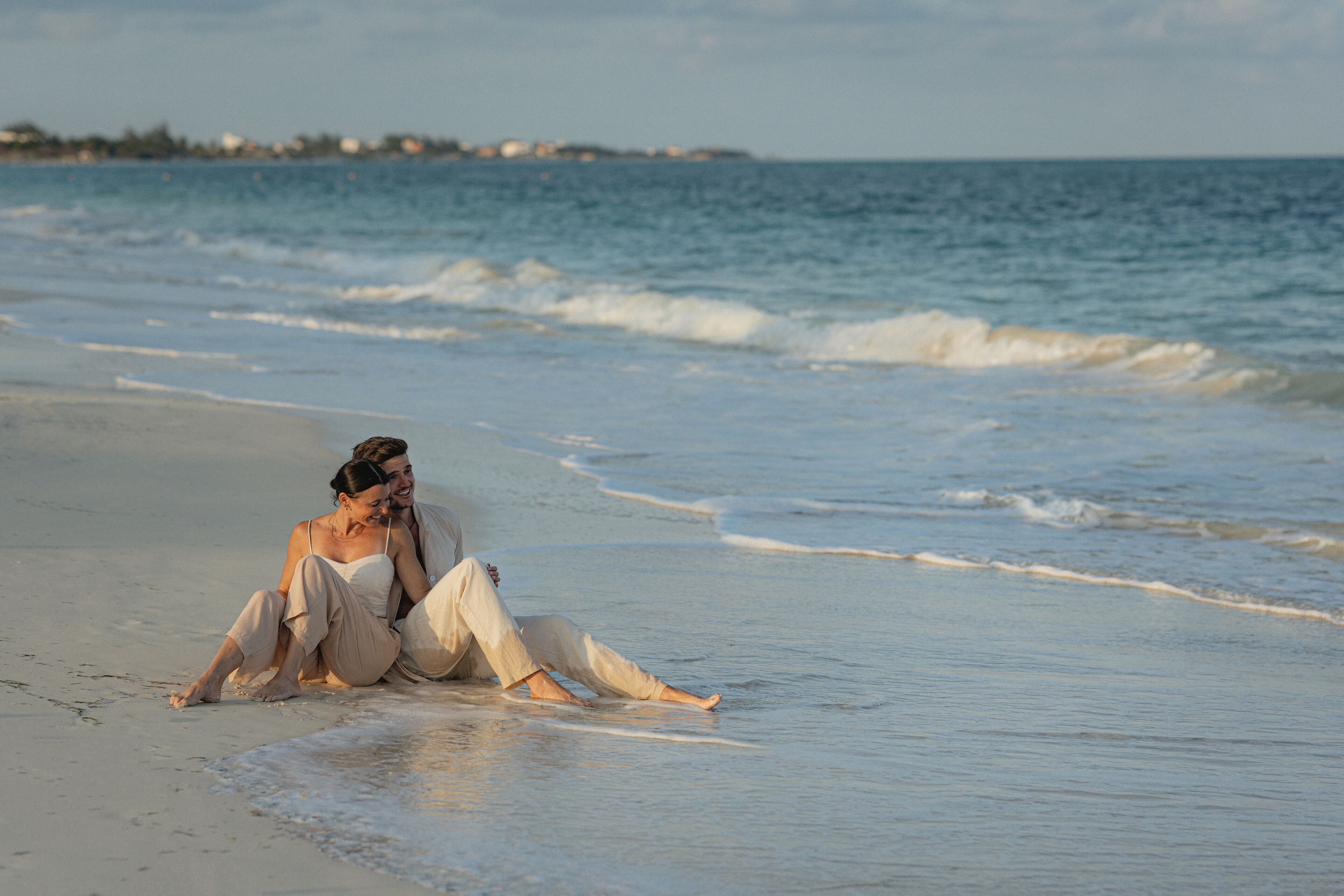 A beach scene with two people sitting on the sand near the water.