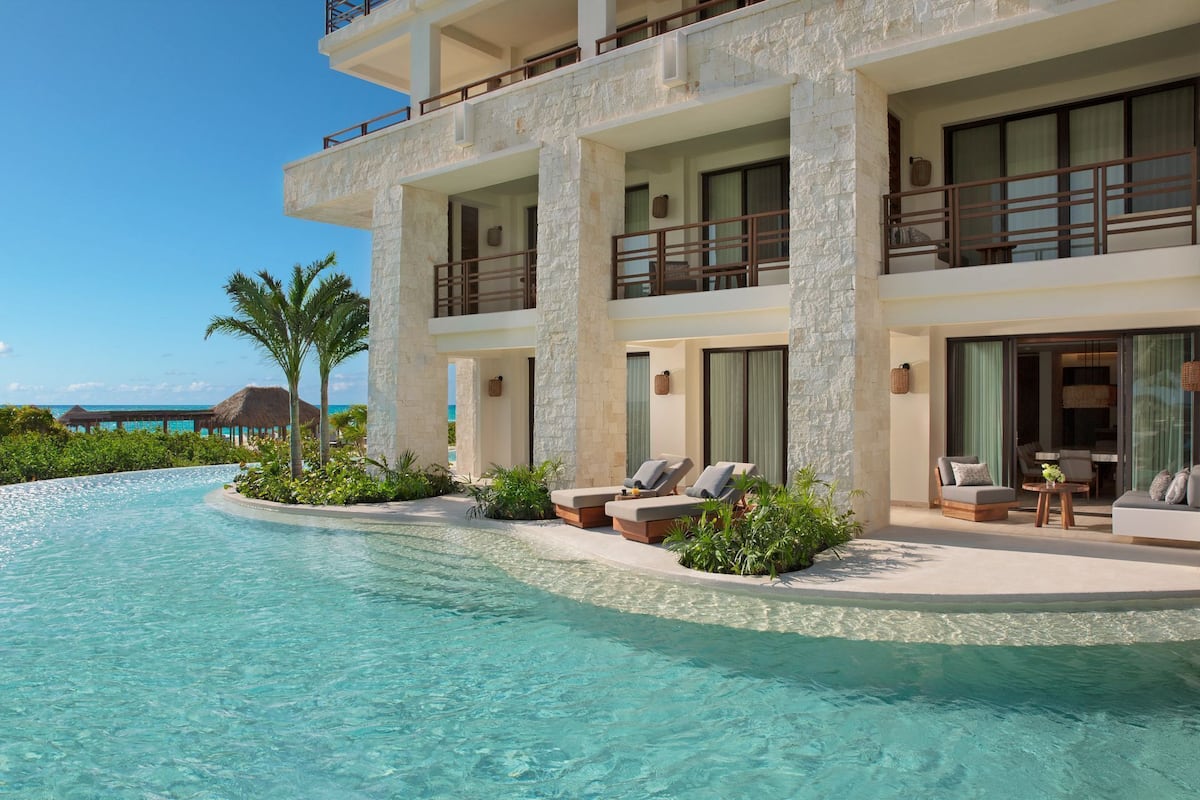 A resort with a pool, lounge chairs, and a view of the ocean.