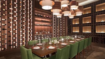 Un espace repas avec une longue table dressée pour le repas, entourée de chaises à l’assise verte.