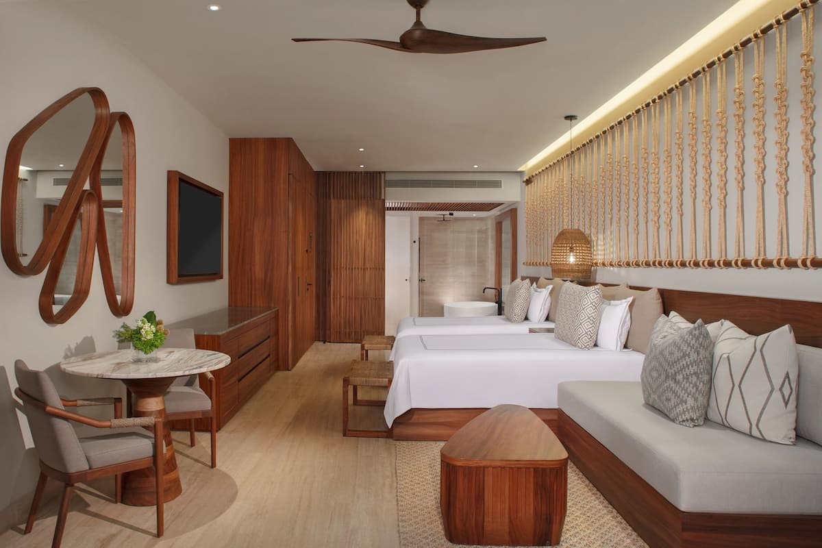 A hotel room with a bed, a sofa, a desk, and a chair. There is a mirror on the wall and a ceiling fan.
