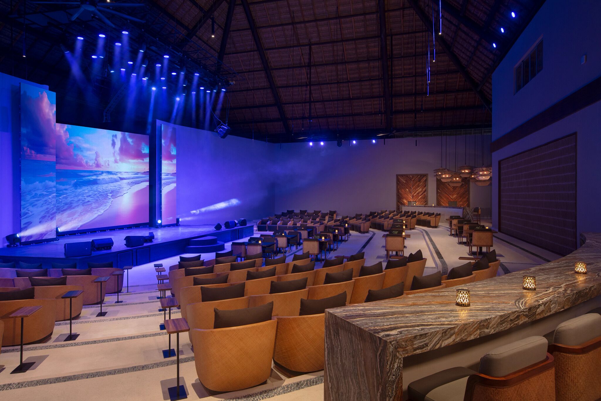 A spacious auditorium with tiered seating, a large screen displaying a scenic image, and ambient lighting.