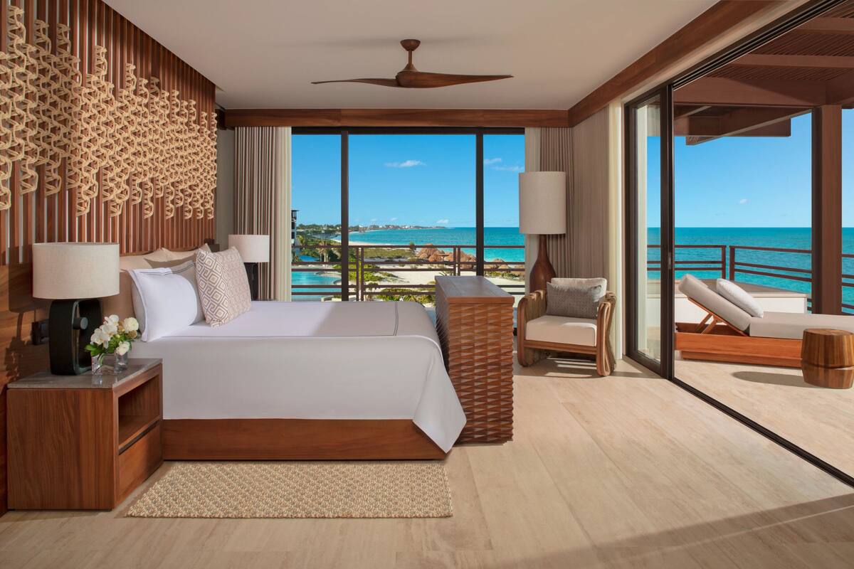 A spacious bedroom with a large bed, a wooden headboard, and a view of the ocean.