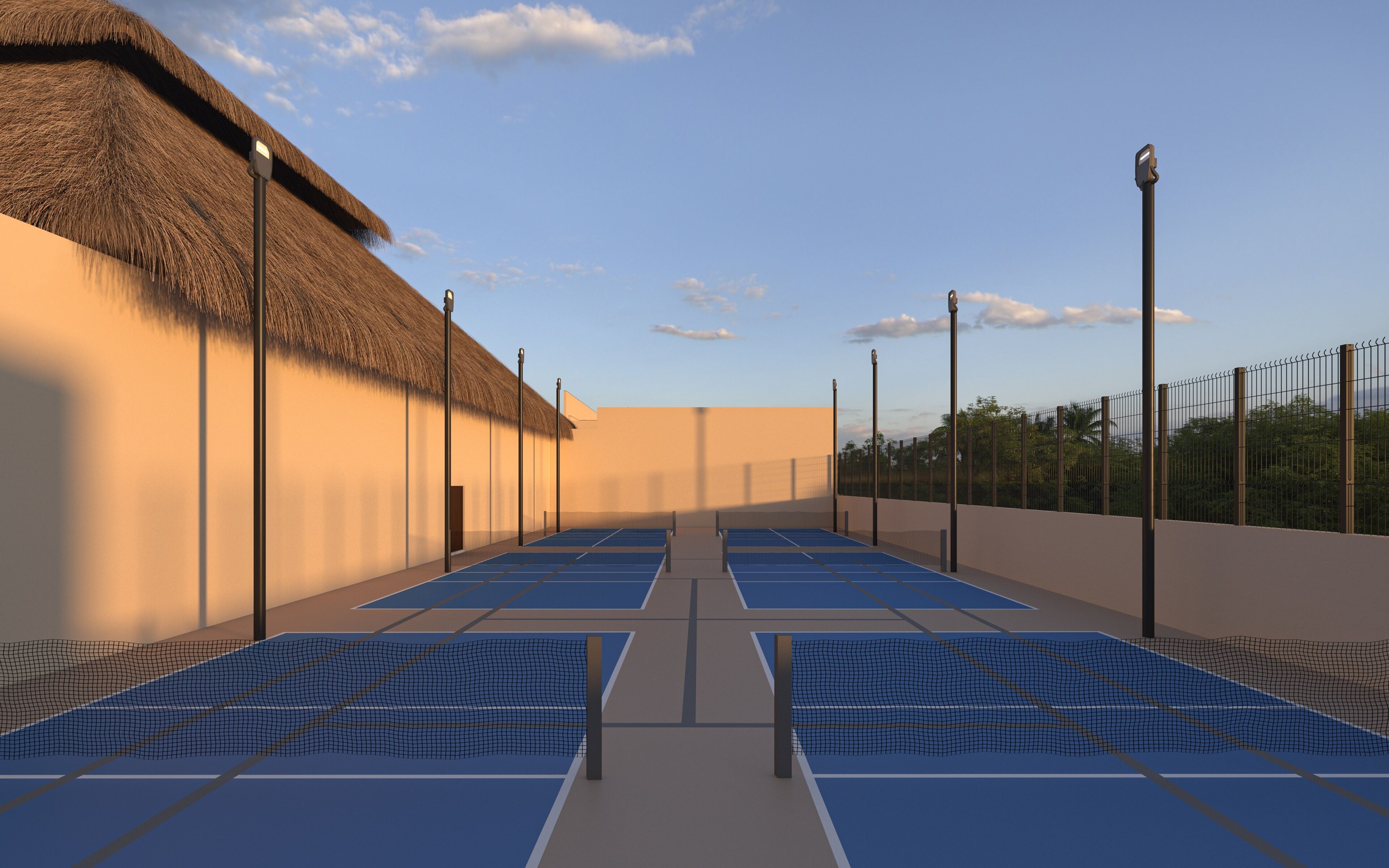 A tennis court with netted boundaries, a thatched roof structure, and a fence with street lamps.
