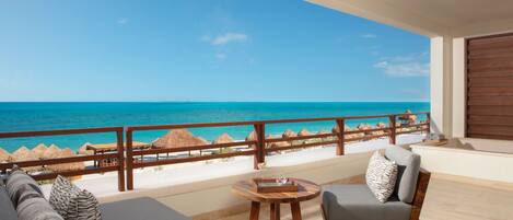 A balcony with a view of the ocean, a wooden table, and a sofa with cushions.