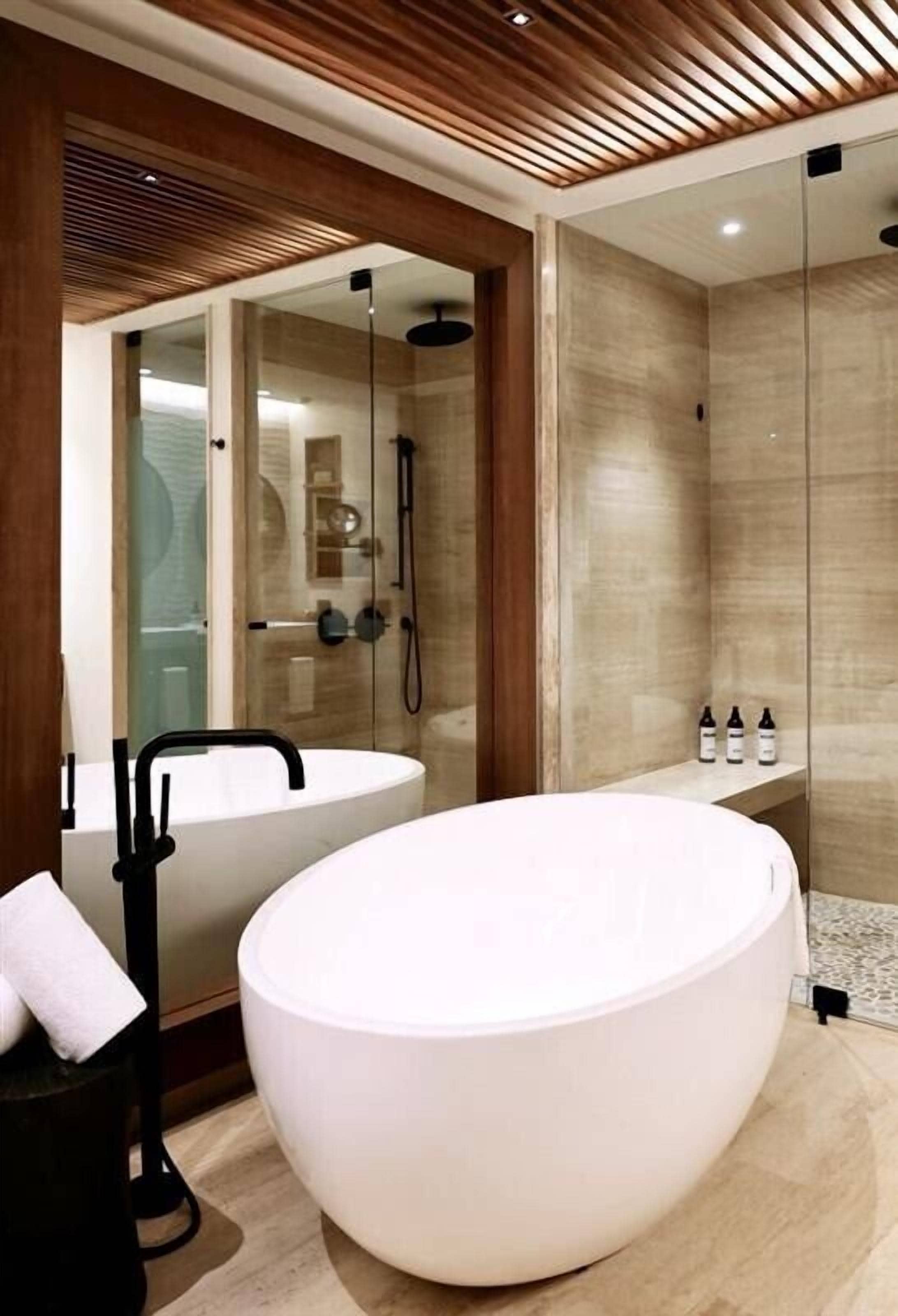 A modern bathroom with a large oval bathtub, a glass-enclosed shower, and a wooden ceiling.