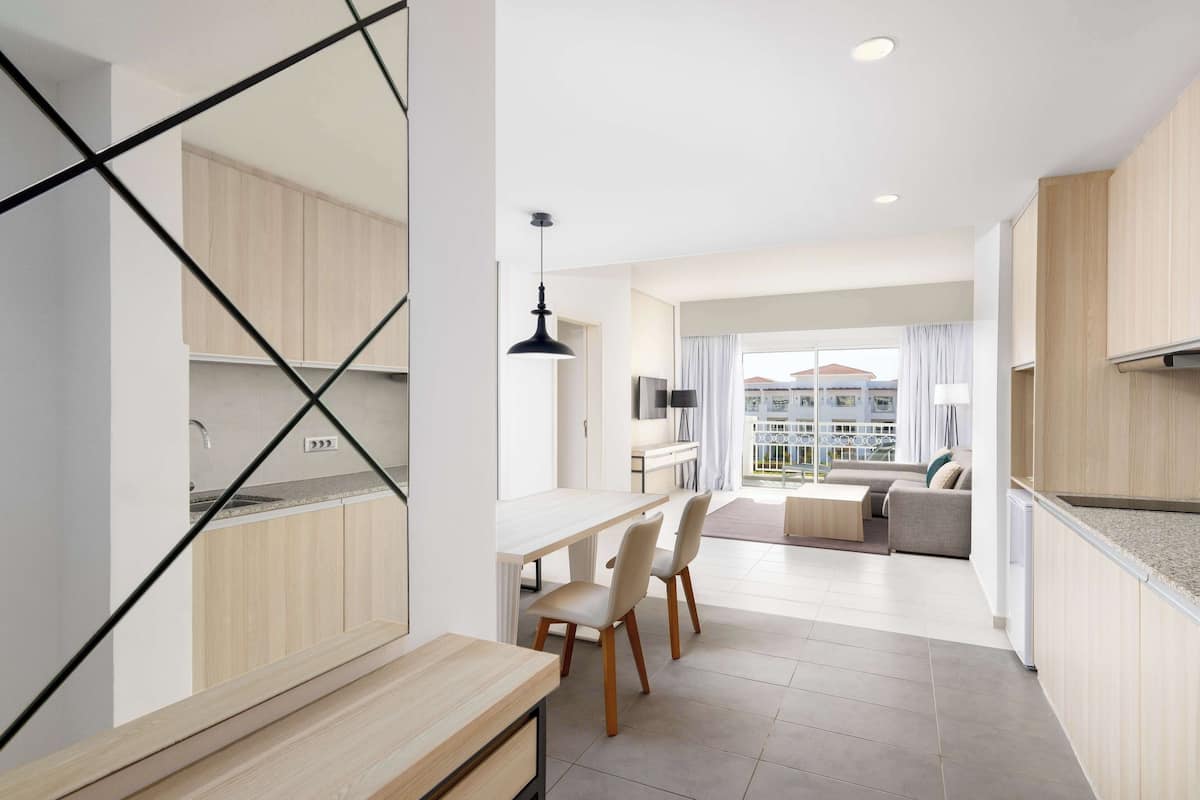 A modern kitchen with wooden cabinets, a dining area with chairs, and a view of a balcony with a sofa.