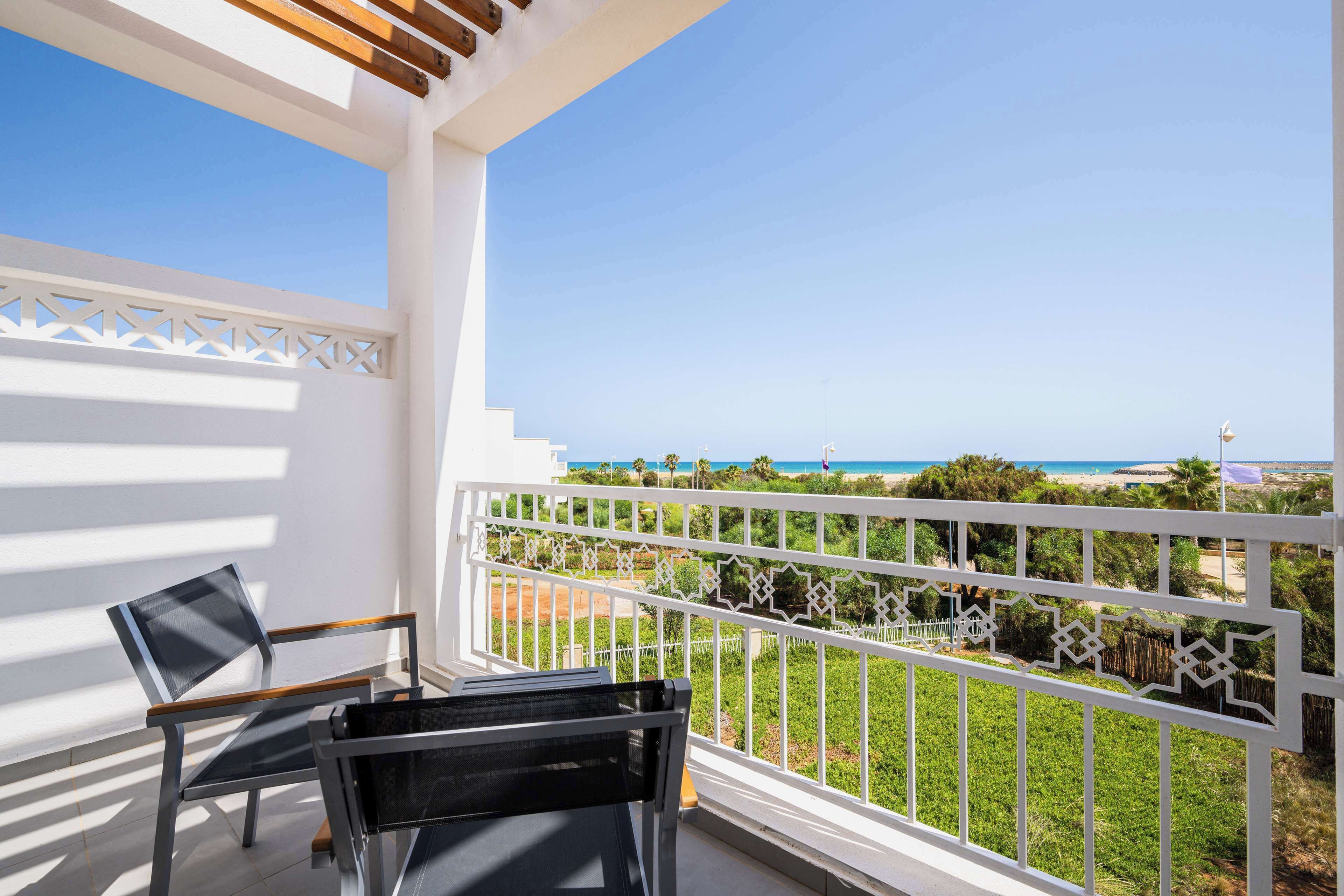 Un balcon offrant une vue sur la plage et l’océan, avec une balustrade blanche et un plafond en bois.