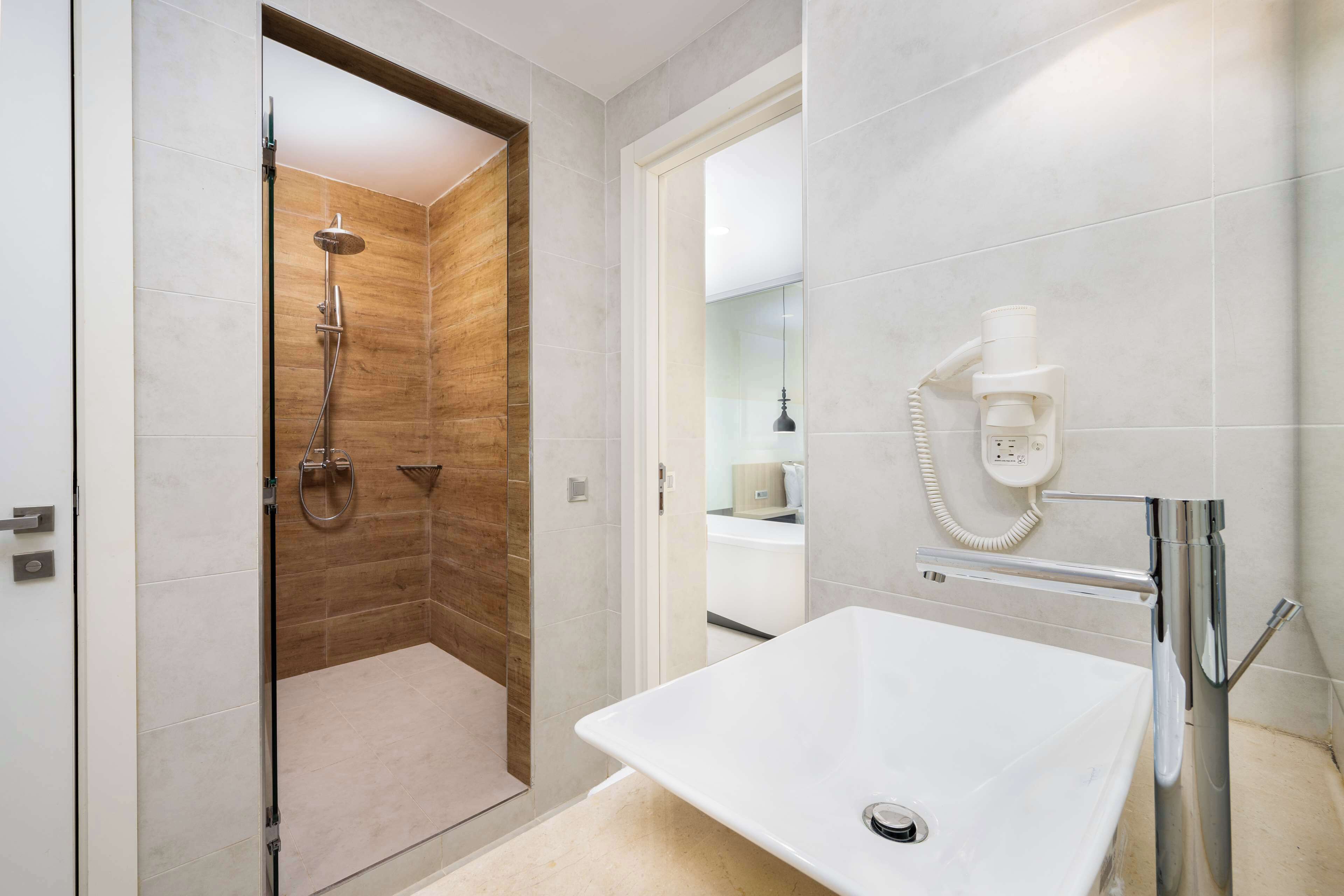 Une salle de bain moderne avec une douche à parois de verre, un lavabo blanc et un sèche-cheveux fixé au mur.