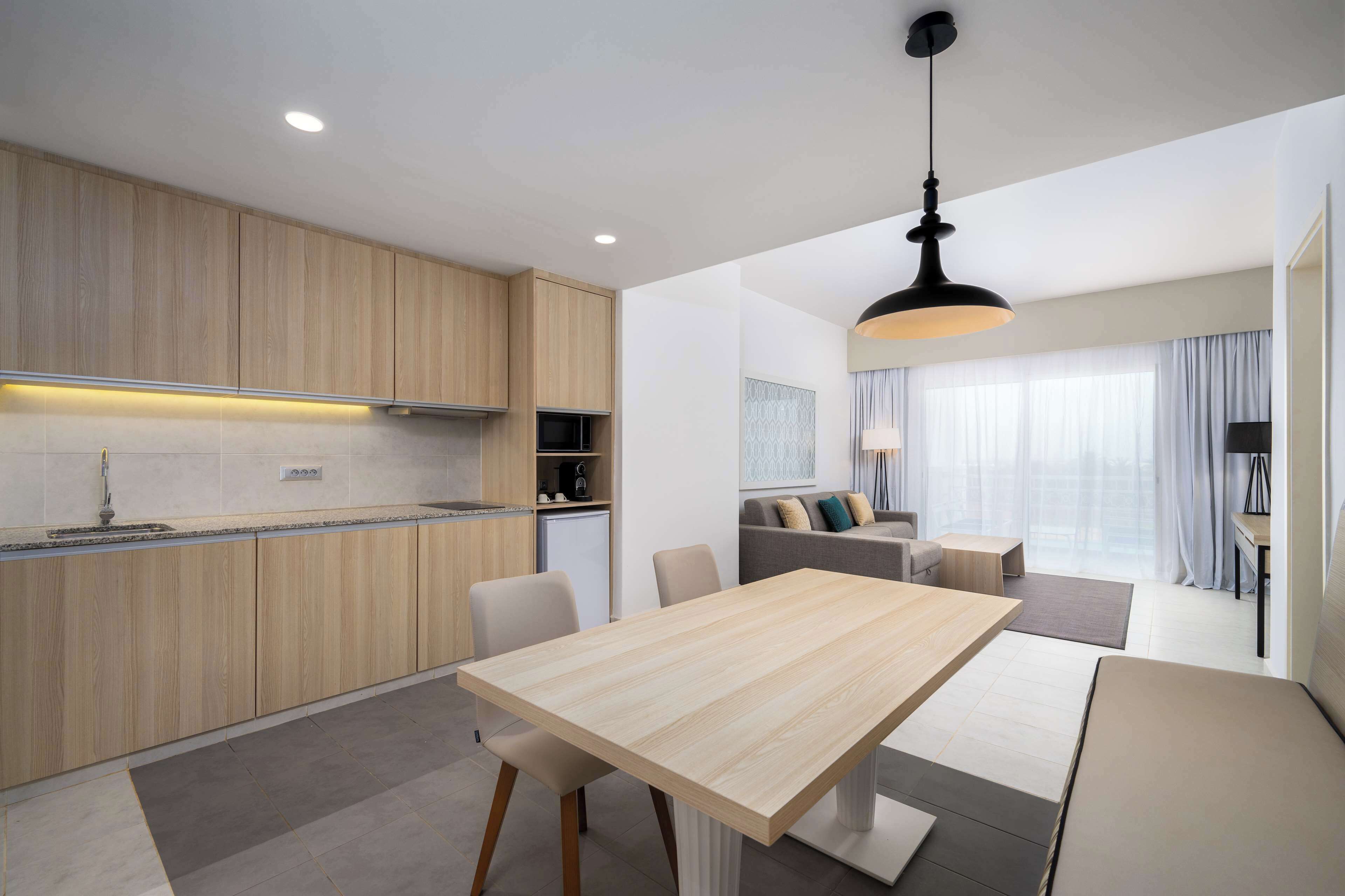 Una cocina moderna con armarios de madera, una mesa de comedor y una sala de estar con sofá y televisor.