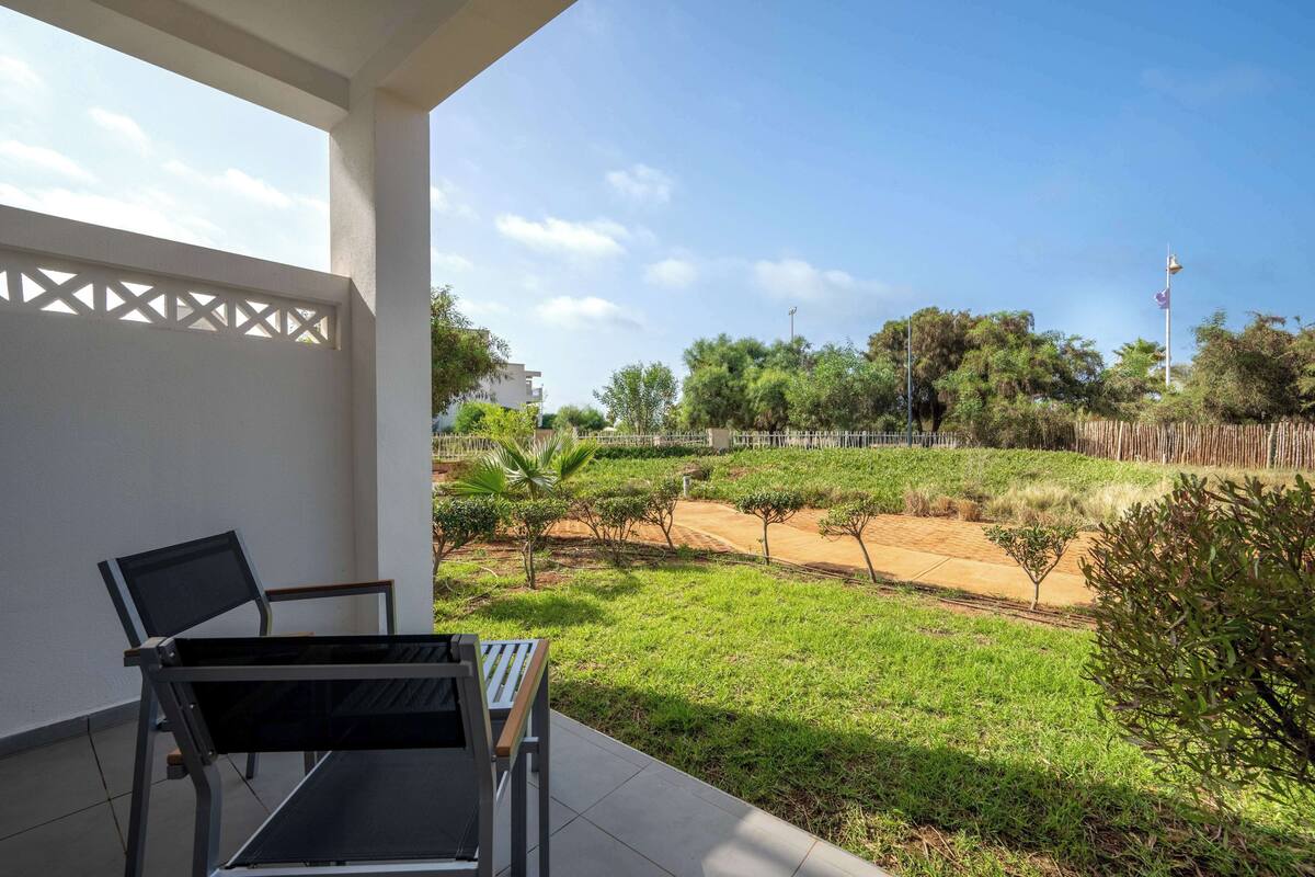 A patio with a table and chairs, a view of a landscaped garden, and a clear sky.
