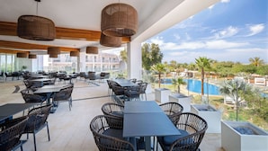 An outdoor dining area with wicker furniture and hanging lights, overlooking a pool and greenery.
