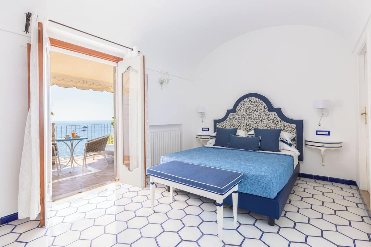 Un dormitorio con cama, un banco, una mesita de noche y vistas al mar.