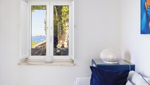 A room with a large window offering a view of the sea and rocky landscape. - Villa Nannina (Positano)