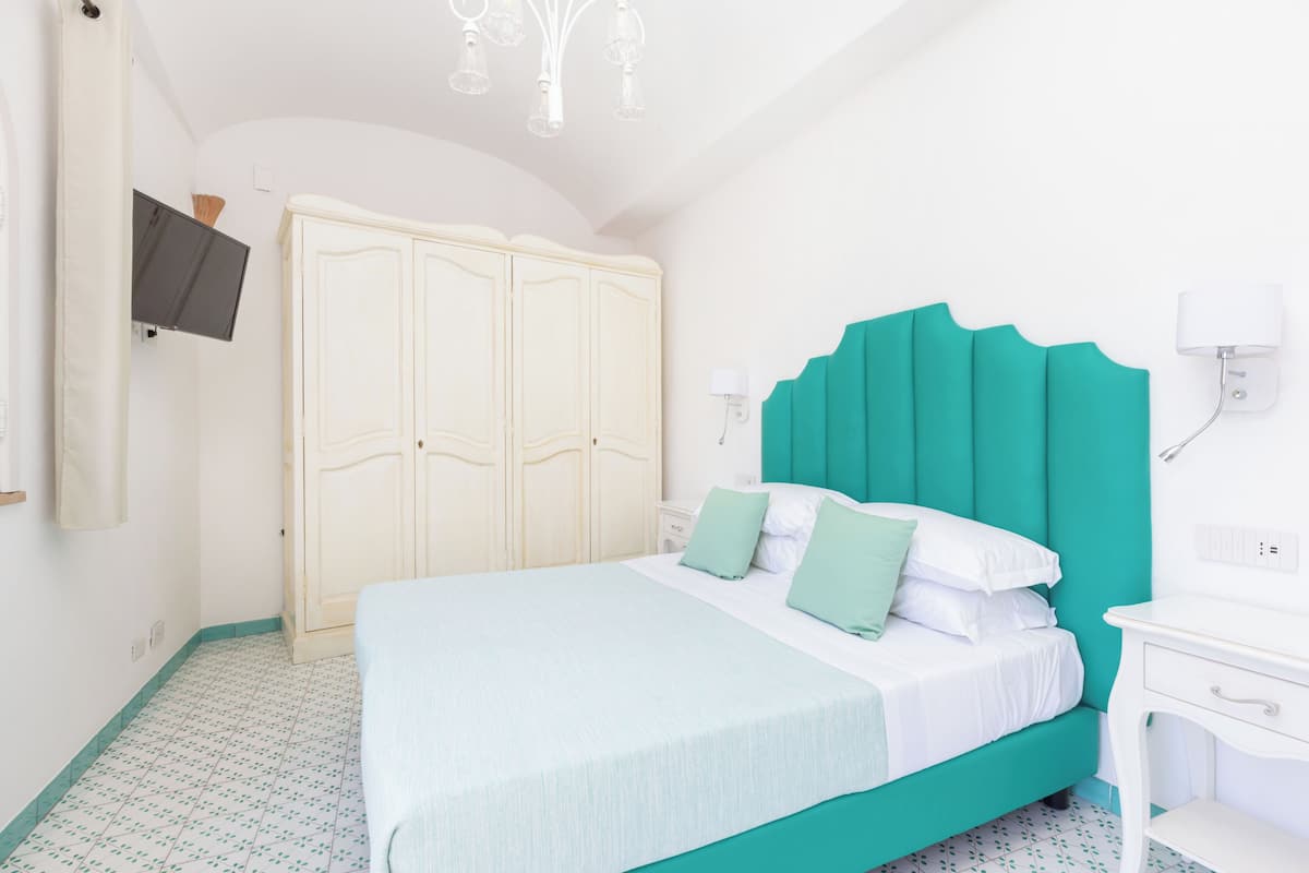 Un dormitorio con cama, armario, mesita de noche y televisor instalado en la pared.