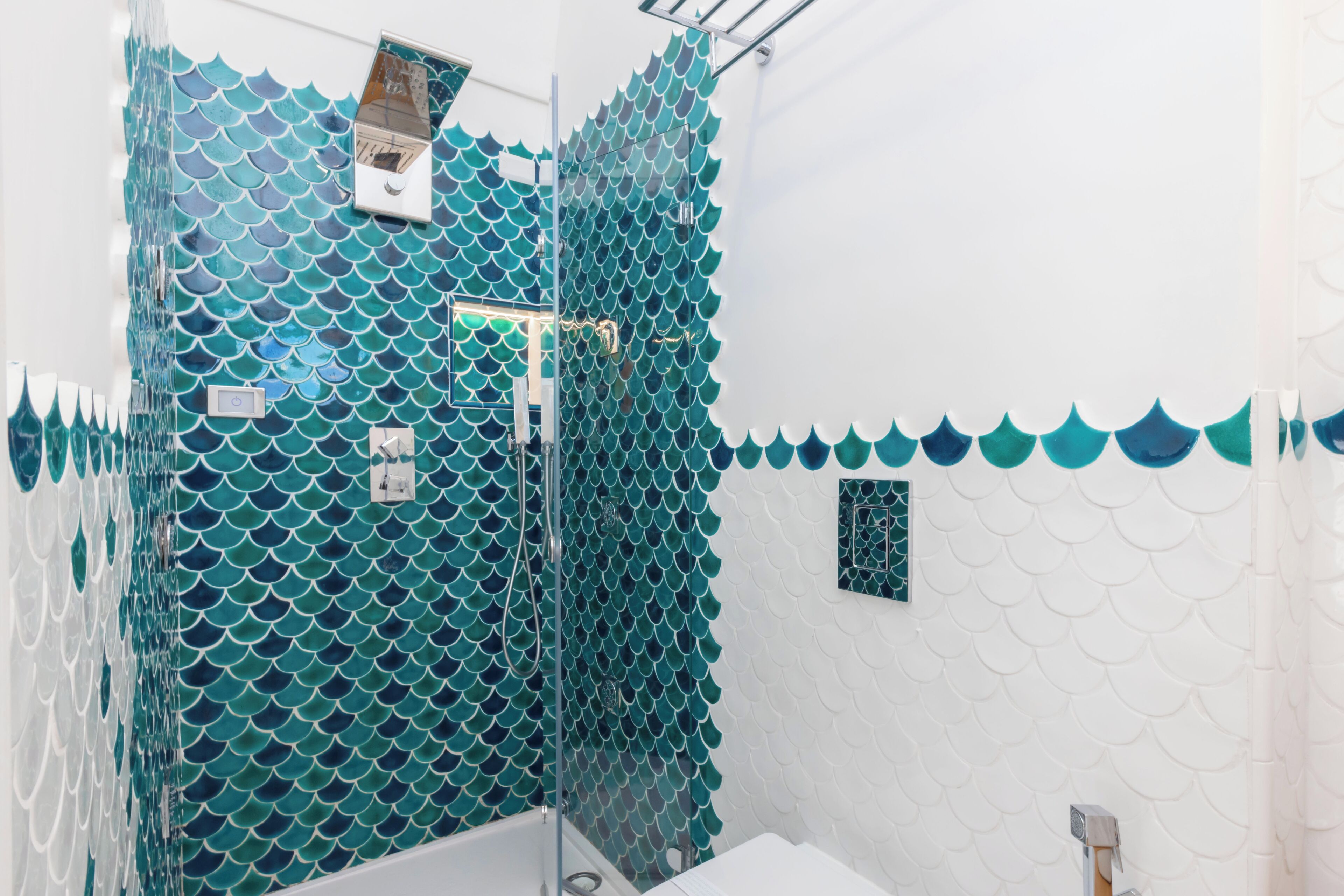 A bathroom with a shower area featuring a blue, fish-scale patterned wall.