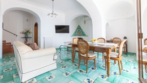 A dining area with a wooden table and chairs, a TV mounted on the wall, and a Christmas tree. - Villa Nannina (Positano)
