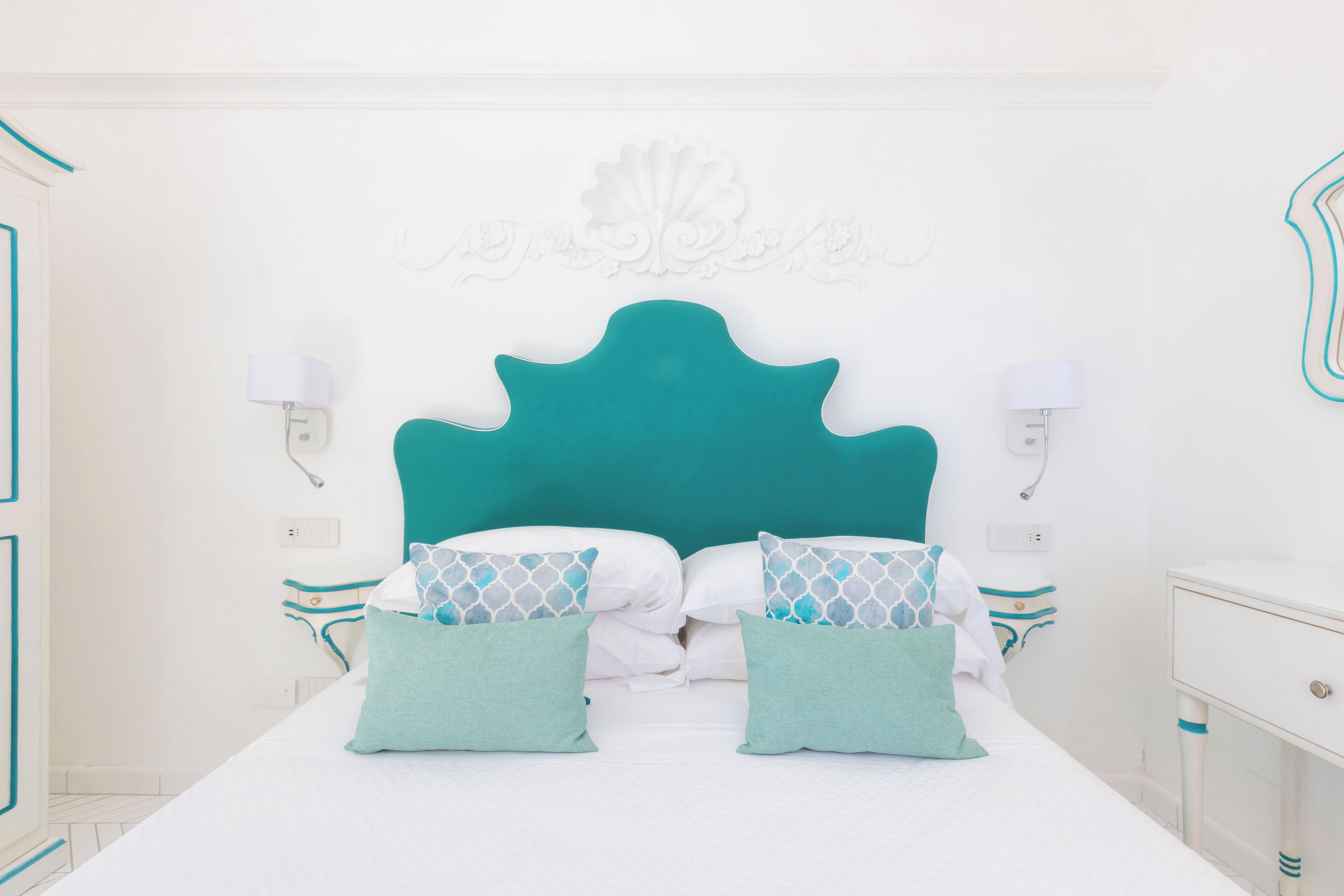 Un lit bien fait, avec une literie aux tons turquoise et blanc, une tête de lit turquoise et des éléments de décoration murale assortis.