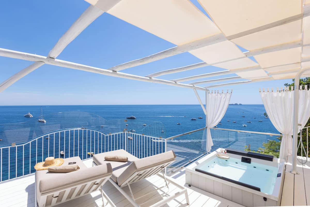 Un balcón con barandillas blancas, un jacuzzi y sillones de descanso con vistas al mar.