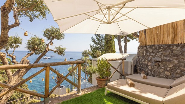 A terrace with a stone wall, a sofa, and an umbrella. - Villa Nannina (Positano)