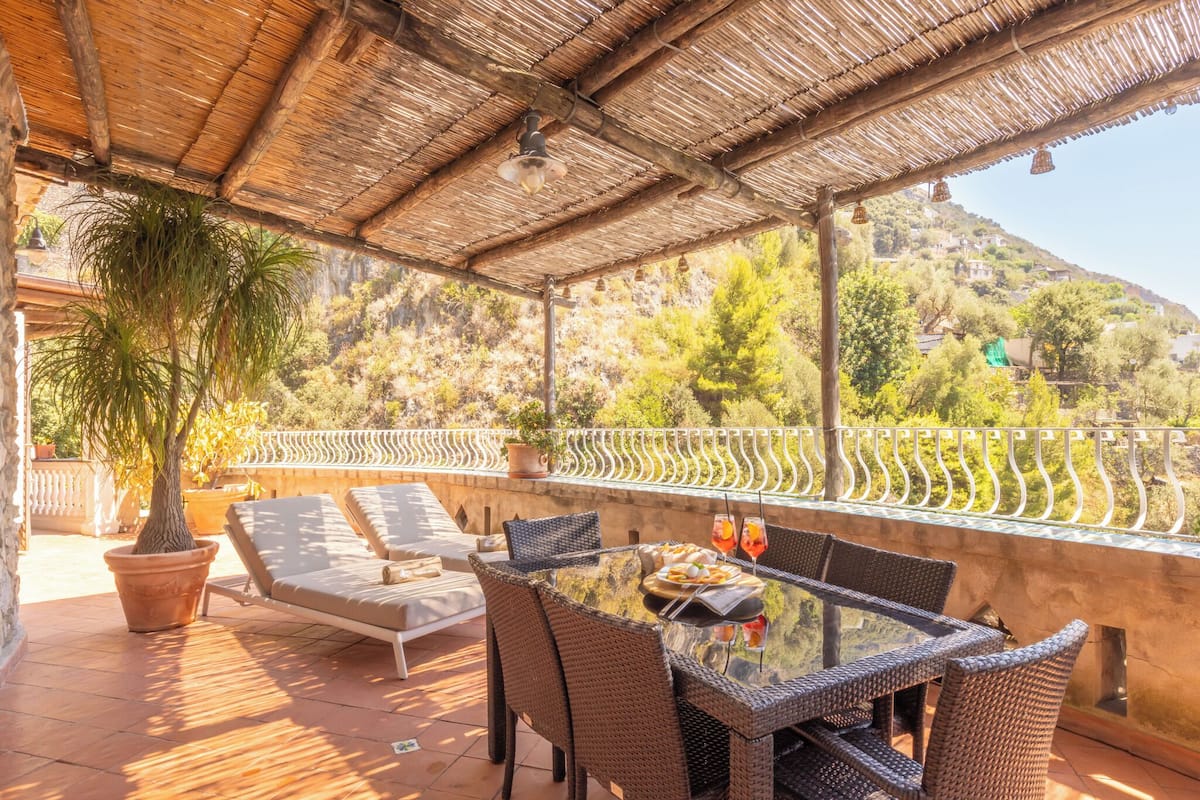Un patio exterior con mobiliario de mimbre, una mesa y una planta en maceta.