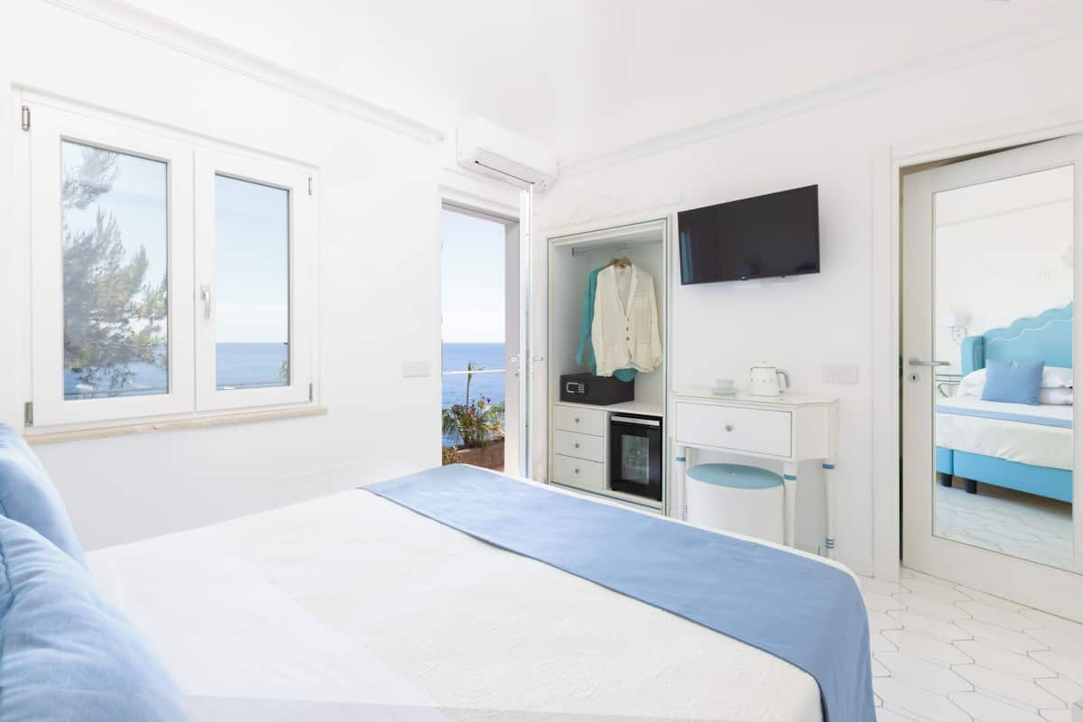Un dormitorio con cama, televisor montado en la pared, armario y vista al mar a través de una ventana.
