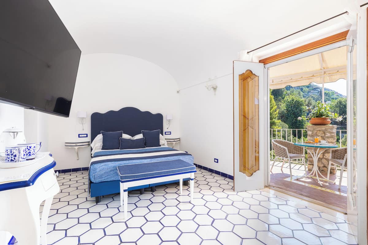 Un dormitorio con cama, mesitas de noche, televisor y balcón con mesa y sillas.