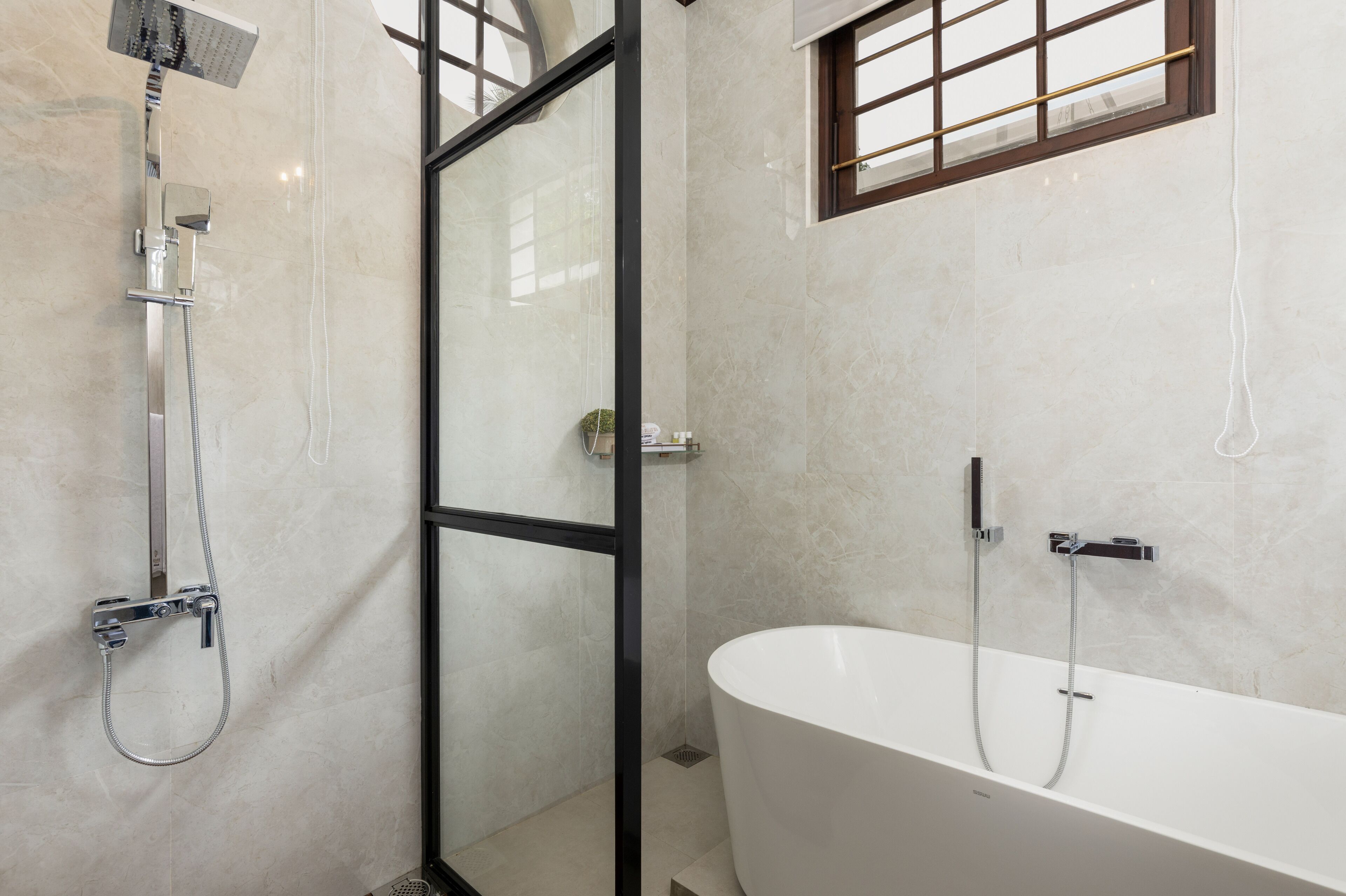 A modern bathroom with a freestanding bathtub, a glass-enclosed shower area, and a window with a grid pattern.