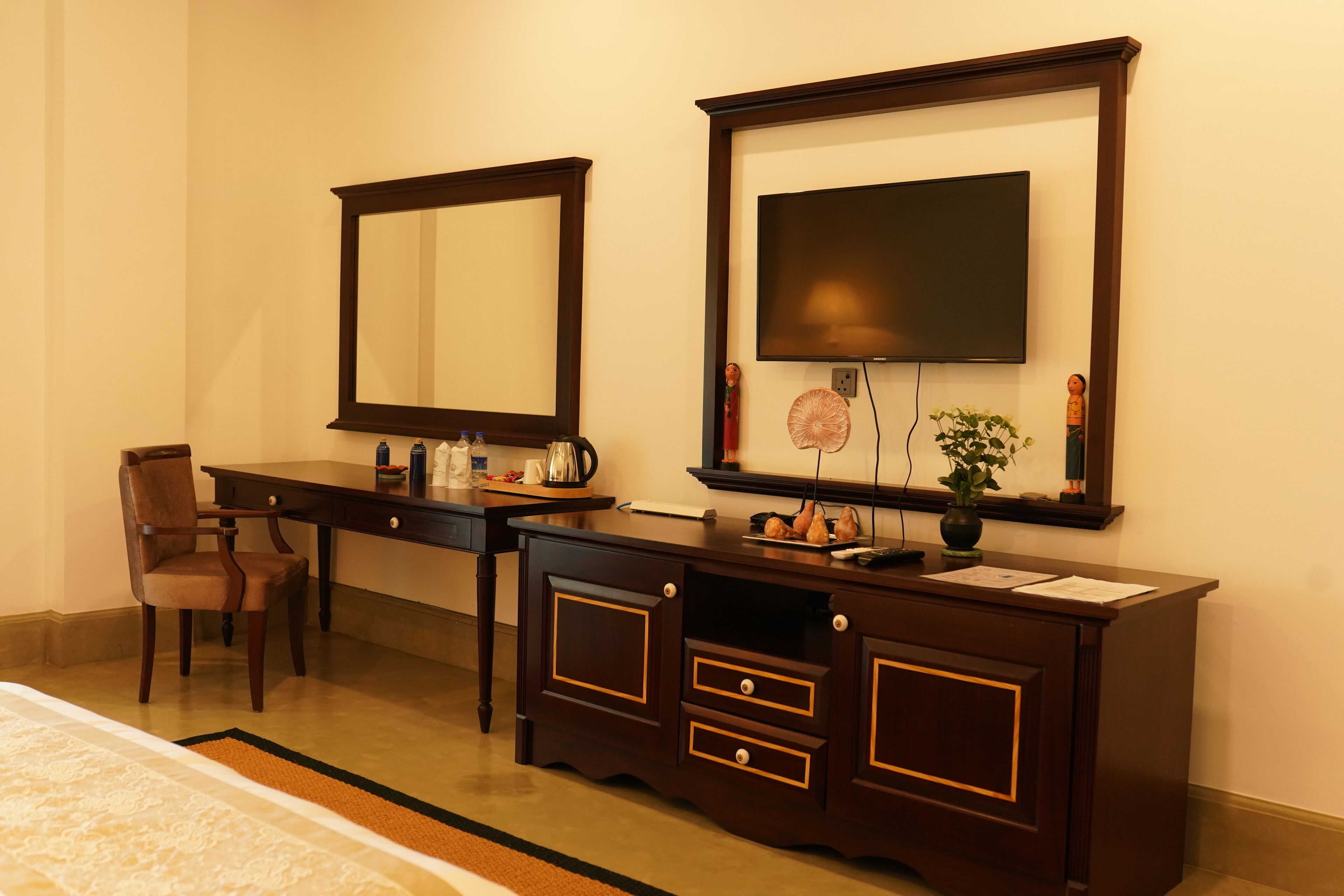 A hotel room with a large bed, a wooden dresser with a mirror, a television, and a small plant.