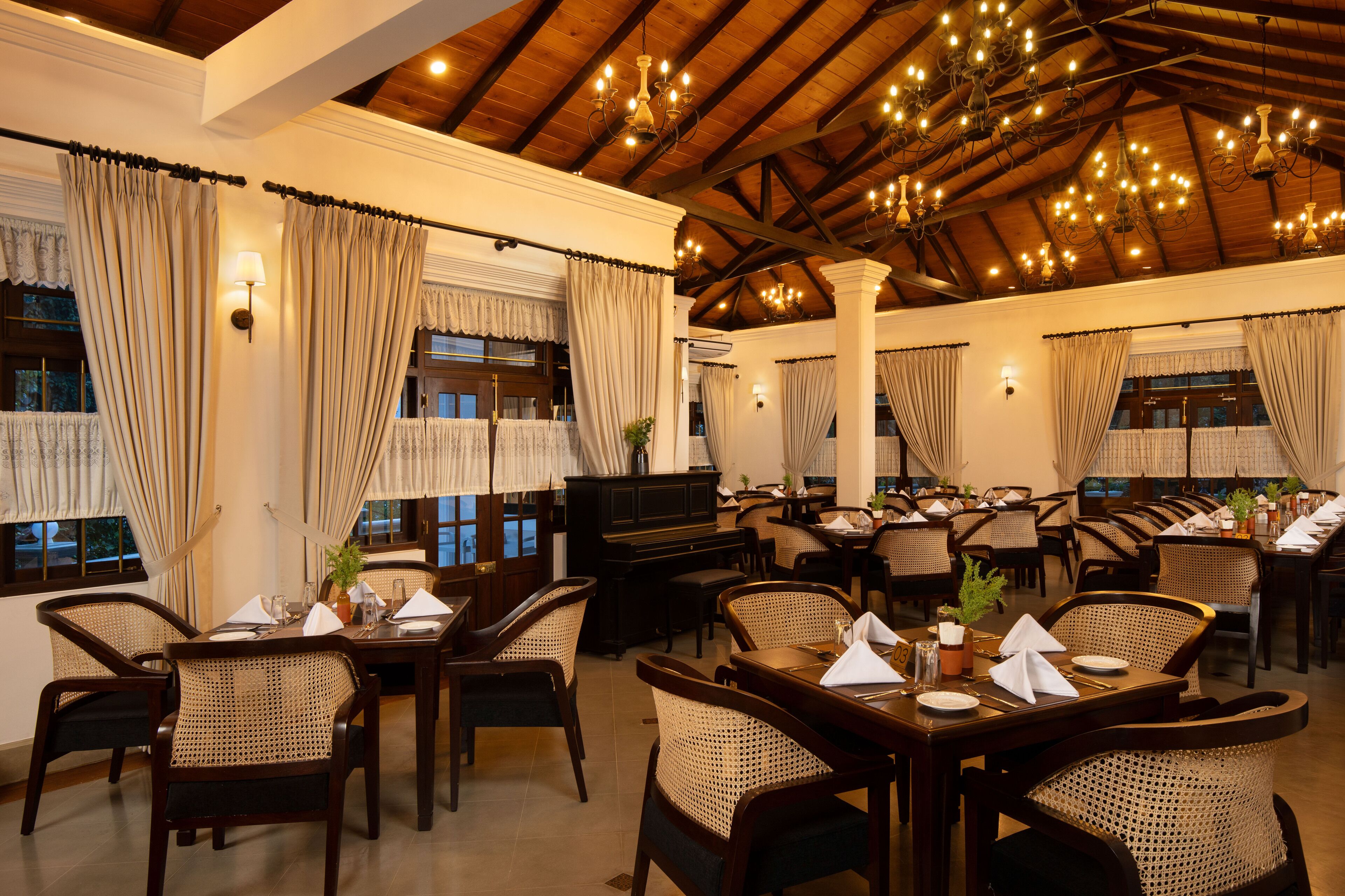 A restaurant with wooden tables and chairs, chandeliers, and curtains.