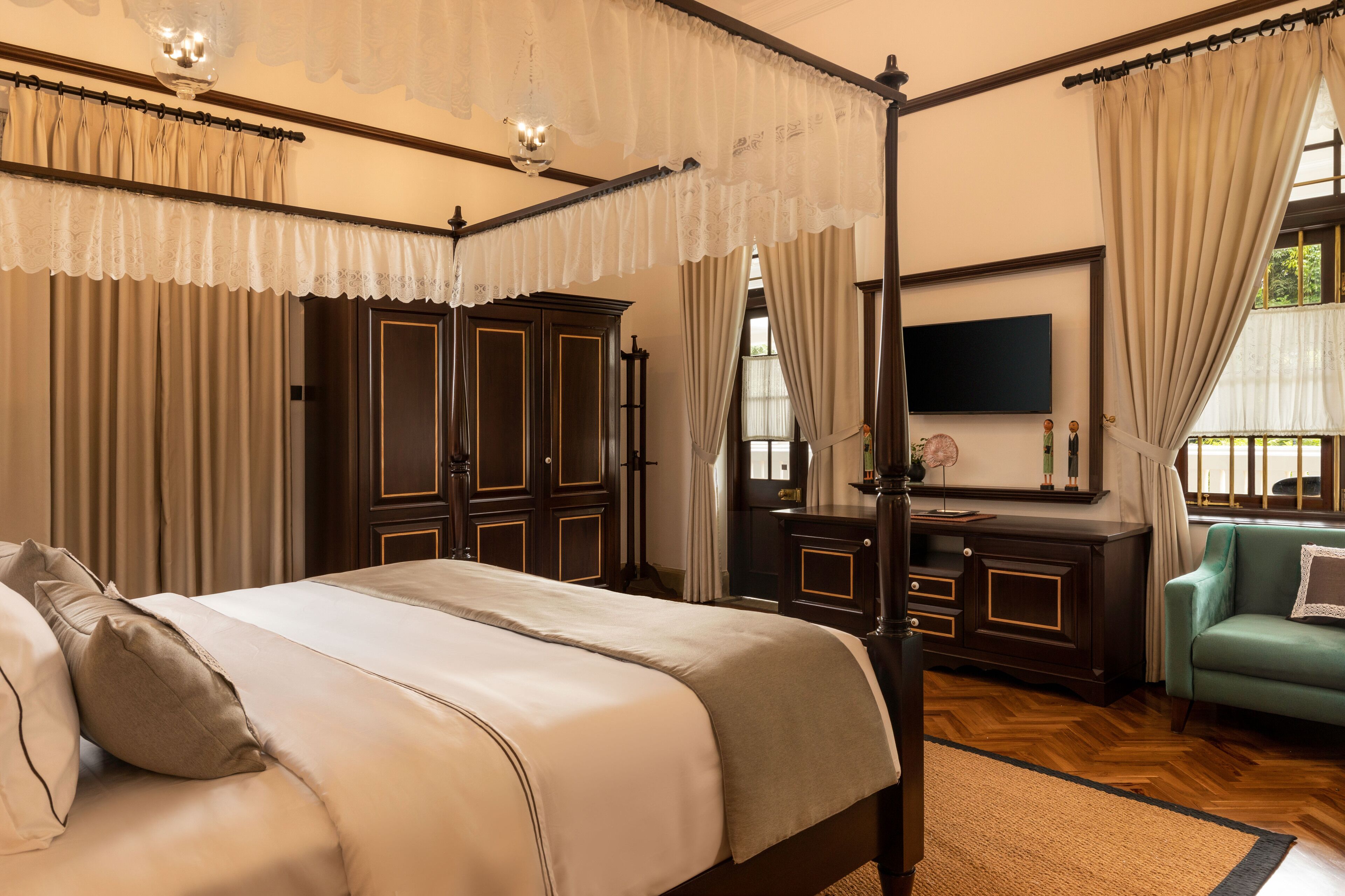 A four-poster bed with a canopy, a television mounted on the wall, and a green armchair.